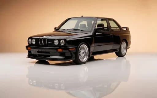 BMW M3 E30 noire de 1990, coupé de collection vu de trois quarts avant en studio sur fond beige, jantes BBS d'origine